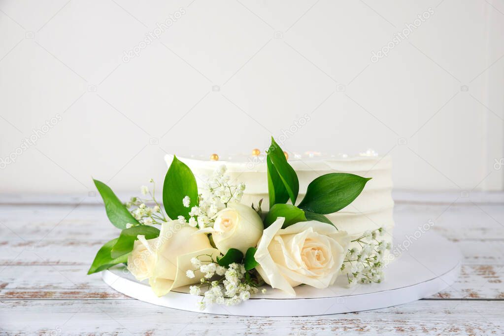 Birthday cake with white roses on white wooden background.