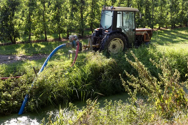 Small tractor with water pump pumps water from ditch for spraying the fruit trees in the Betuwe in Lienden in Gelderland in The Netherlands