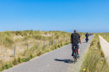 Hollanda 'nın Hollanda kıyılarında Hollanda' daki Okul ve Petten arasında bisiklet süren insanlar var.