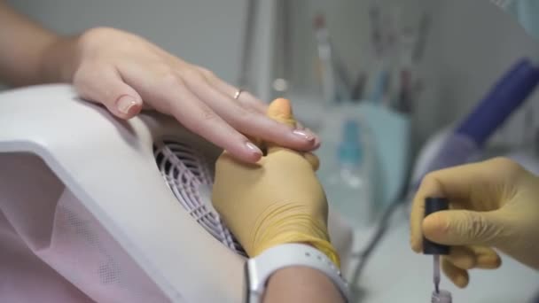 Manicurist i latexhandskar applicerar varsamt ett transparent lager på naglarna — Stockvideo