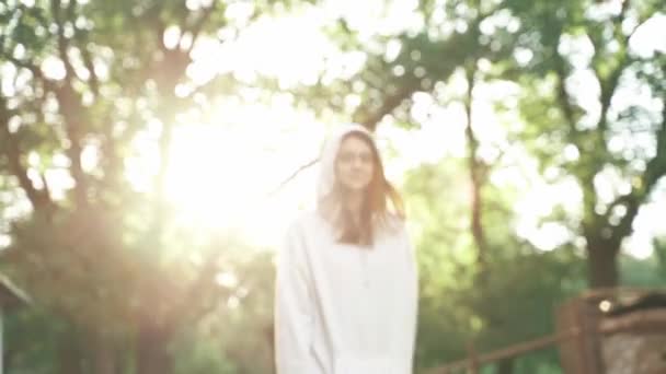 Os raios de sol através dos quais uma menina em um capuz passa e acena sua mão — Vídeo de Stock