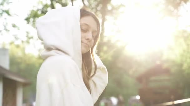 Vacker kvinna i vit luvtröja rätar ut håret vid solnedgången — Stockvideo