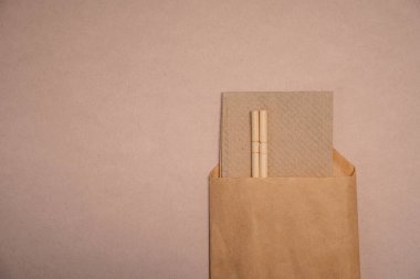 Çin çubukları bej arkaplandaki el işi kağıt ambalajlarından sarkıyor.