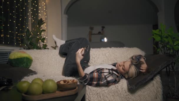 Jolie jeune femme se couche sur le canapé et prend un selfie au téléphone — Video