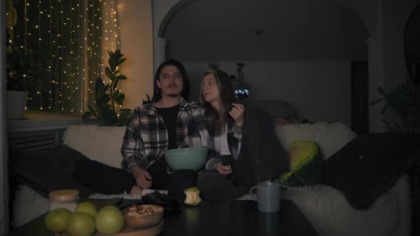 Vänner i rutiga skjortor sitta hemma och titta på en film, äta läckra chips — Stockvideo