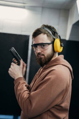 Bir adam ateş etmeden önce bir hedefe nişan alır. Özel kıyafet - balistik kulaklıklar.