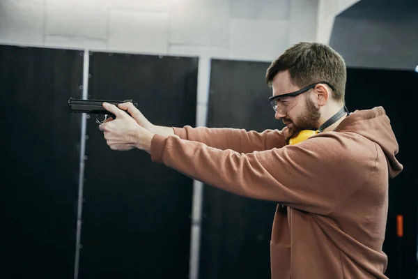 A man stands in the correct position for shooting and prepares to hit the target, holds a pistol in his hands, shooting at a shooting range