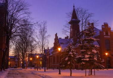 Klaipeda, Litvanya - 01: 15: Eski tarihi Neo-Gotik Üniversitesi kış karı altında kampüs, pembe günbatımı renkleri ve şehir ışıkları. Kartpostallar ve turistik broşürler için bir masal atmosfer fotoğrafı..