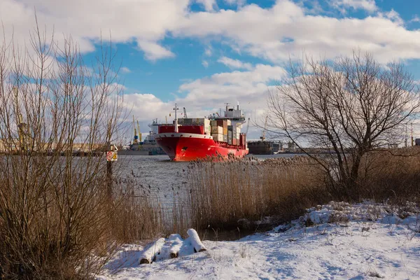 Klaipeda, Litvanya - 02 06 21: Kışın Curonian lagünündeki devasa kırmızı kargo konteynır gemisi terminal sanayi arazisinin önünde. İp ucu bulutlu gökyüzü ile güneşli fotoğraf, ön planda kar ve kadın.
