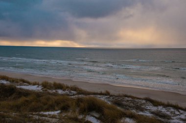 Baltık Denizi Curonian tükürük plajında kış. Kum, koyu mavi deniz, sarı çimenler, don ve dramatik bulutlu gökyüzü ile kaplı kış kumulları. Etrafta kimse yok, üzgün ve depresif.