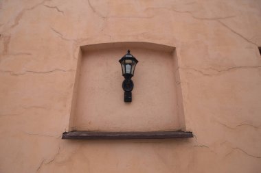 Eski moda, sarı kahverengi alçı alçı bir duvarda sokak lambası.