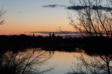 Dinyeper nehrinde gün batımı. Güzel turuncu bulutlu gökyüzü, şehir ve kilise siluetleri nehire yansıyor. Rechytsa, Belarus 'ta güzel bir bahar fotoğrafı çekildi..