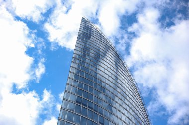 Soyut modern gökdelen mimarisini kapatın. Arka planda bulutlar olan uzun cam bina. Fotoğraf, sıcak bulutlu bir yaz gününde çekildi..