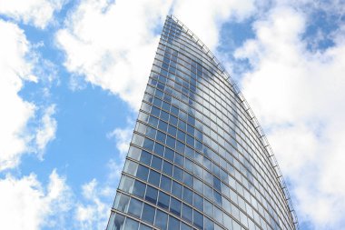 Soyut modern gökdelen mimarisini kapatın. Arka planda bulutlar olan uzun cam bina. Fotoğraf, sıcak bulutlu bir yaz gününde çekildi..