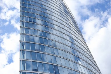 Soyut modern gökdelen mimarisini kapatın. Arka planda bulutlar olan uzun cam bina. Fotoğraf, sıcak bulutlu bir yaz gününde çekildi..