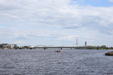 Daugava nehrinin çevresel manzarası ve arka planda ulaşım köprüleri. Fotoğraf, sıcak bir yaz bulutlu bir günde çekildi..