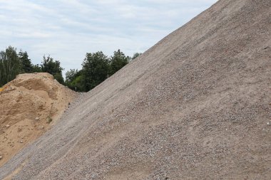 İnşaat alanının ayrıntıları çakıl taşlarıyla dolu, büyük bir yığın halinde. Fotoğraf, sıcak bir yaz gününde bulutlu bir gökyüzü ile çekildi..