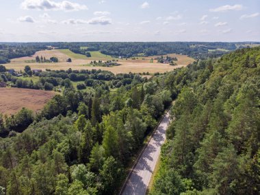 Orman ve tarım alanlarının yakınındaki otobanın insansız hava aracı fotoğrafçılığı. Fotoğraf sıcak ve bulutlu bir yaz gününde çekildi..