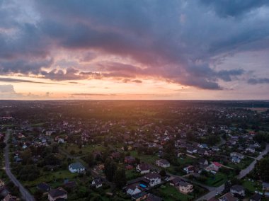 Akşamın geç saatlerinde küçük özel evleri ve bahçeleri olan banliyölerin gerçek gün batımı drone görüntüsü. Fotoğraf, sıcak ve bulutlu bir yaz akşamı çekildi..