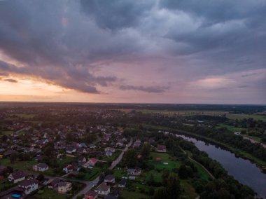 Akşamın geç saatlerinde küçük özel evleri ve bahçeleri olan banliyölerin gerçek gün batımı drone görüntüsü. Fotoğraf, sıcak ve bulutlu bir yaz akşamı çekildi..