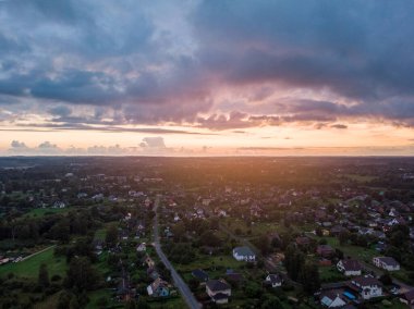 Akşamın geç saatlerinde küçük özel evleri ve bahçeleri olan banliyölerin gerçek gün batımı drone görüntüsü. Fotoğraf, sıcak ve bulutlu bir yaz akşamı çekildi..