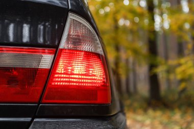 Arka taraf E46 kırmızı araba ışıklarını kapatın. Fotoğraf, arka planda sonbahar renkleri olan bulutlu bir sonbahar gününde çekildi.