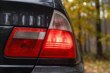 Arka taraf BMW E46 kırmızı araba ışıklarını kapatın. Fotoğraf, arka planda sonbahar renkleri olan bulutlu bir sonbahar gününde çekildi.