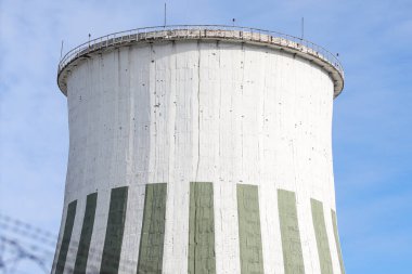 Büyük beyaz baca, endüstriyel elektrikli kule manzaralı ve önünde dikenli teller olan bina. Fotoğraf, sıcak ve bulutlu bir sonbahar gününde mavi gökyüzü ile çekildi..