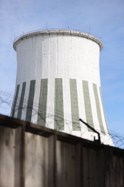 Büyük beyaz baca, endüstriyel elektrikli kule manzaralı ve önünde dikenli teller olan bina. Fotoğraf, sıcak ve bulutlu bir sonbahar gününde mavi gökyüzü ile çekildi..