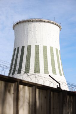 Büyük beyaz baca, endüstriyel elektrikli kule manzaralı ve önünde dikenli teller olan bina. Fotoğraf, sıcak ve bulutlu bir sonbahar gününde mavi gökyüzü ile çekildi..