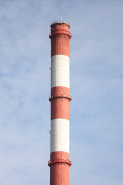 Tall, thin Two Color red and white chimney on the background of blue sky with clouds. Photo taken on a warm overcast autumn day.