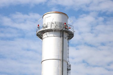 Small silver color electric plant chimney. Photo taken on a sunny autumn day with many small clouds in the background.