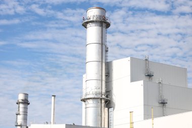 Small silver color electric plant chimney. Photo taken on a sunny autumn day with many small clouds in the background.