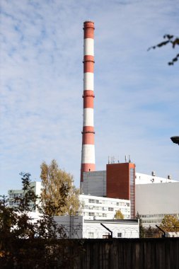 Tall, thin Two Color red and white chimney on the background of blue sky with clouds. Photo taken on a warm overcast autumn day.