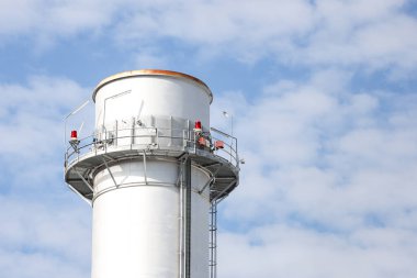 Small silver color electric plant chimney. Photo taken on a sunny autumn day with many small clouds in the background.