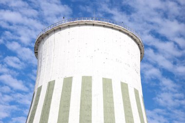 Close-up photo of large industrial factory chimney. Photo taken on the foreground of blue sky and white clouds.