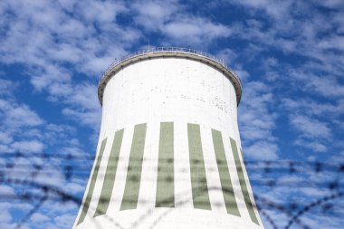 Large power plant white chimney with  unsharp barbed wires in foreground. Photo taken on a warm overcast autumn day.