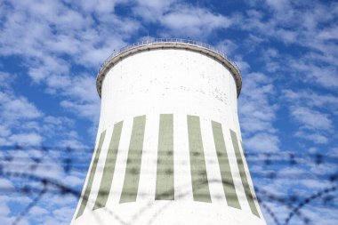 Large power plant white chimney with  unsharp barbed wires in foreground. Photo taken on a warm overcast autumn day.