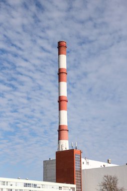 Large, tall electricity thermal power plant red, white color chimney building factory. Photo taken on a warm overcast autumnd ay with blue sky and white clouds.