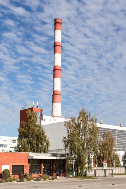 Large, tall electricity thermal power plant red, white color chimney building factory. Photo taken on a warm overcast autumnd ay with blue sky and white clouds.