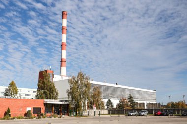 Large, tall electricity thermal power plant red, white color chimney building factory. Photo taken on a warm overcast autumnd ay with blue sky and white clouds.