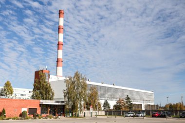 Large, tall electricity thermal power plant red, white color chimney building factory. Photo taken on a warm overcast autumnd ay with blue sky and white clouds.