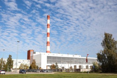 Large, tall electricity thermal power plant red, white color chimney building factory. Photo taken on a warm overcast autumnd ay with blue sky and white clouds.