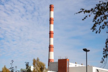 Tall, thin Two Color red and white chimney on the background of blue sky with clouds. Photo taken on a warm overcast autumn day.