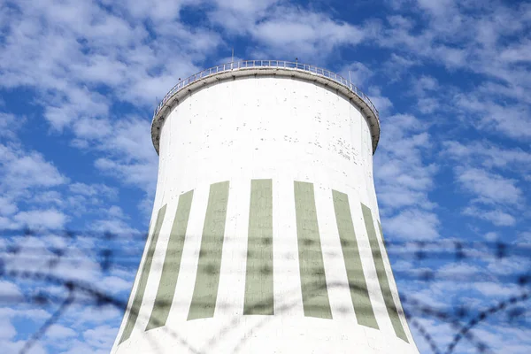 Large power plant white chimney with  unsharp barbed wires in foreground. Photo taken on a warm overcast autumn day.