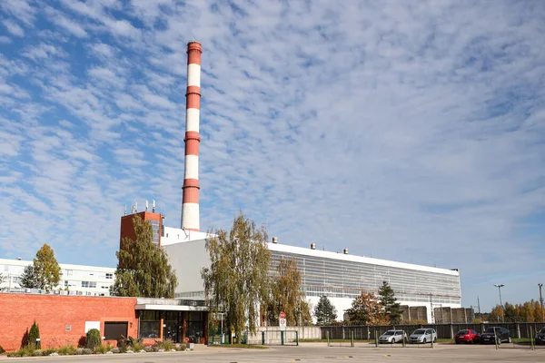 Large, tall electricity thermal power plant red, white color chimney building factory. Photo taken on a warm overcast autumnd ay with blue sky and white clouds.