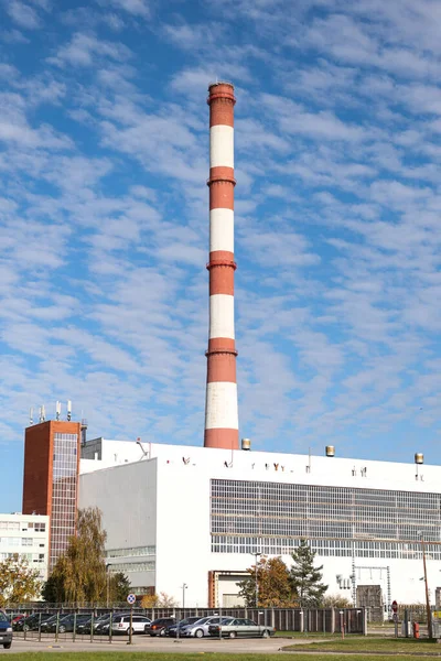 Large, tall electricity thermal power plant red, white color chimney building factory. Photo taken on a warm overcast autumnd ay with blue sky and white clouds.