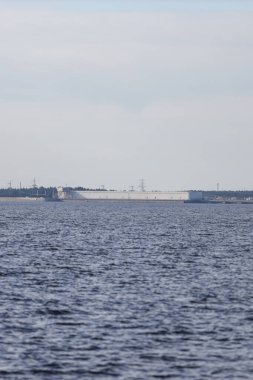 Large river view with large seawall, dam in background. Photo taken on a warm autumn day. Overcast, cloudy weather.