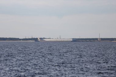 Large river view with large seawall, dam in background. Photo taken on a warm autumn day. Overcast, cloudy weather.