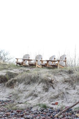 Kum kıyısına ve Baltık sahiline yakın dört tahta koltuk. Fotoğraf, sıcak bir bulutlu günde çekildi..